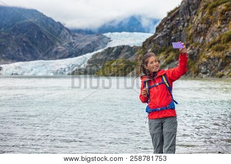 Tourist woman taking selfie photo at Mendenhall glacier in Juneau, Alaska. Famous tourism destination on Alaska cruise, USA travel.