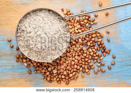 measuring scoop of gluten free  buckwheat flour with kasha grain against wooden background