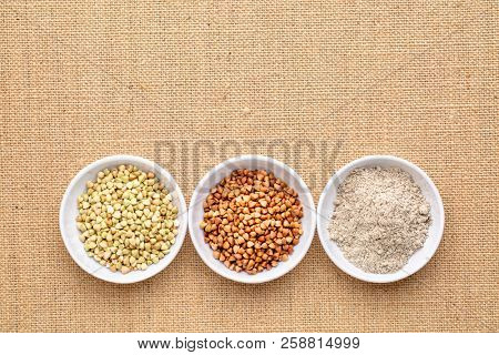 gluten free buckwheat groats, roasted kasha and flour - a row of small ceramic bowls against burlap canvas