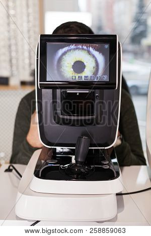 Ophthalmologist Examining Young Man With Optometric Machine In Optics Store