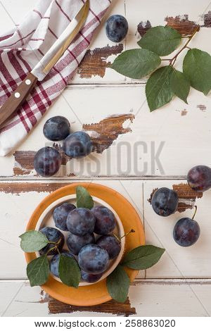 Fresh Plum Berries On A Plate With Leaves On A Light Table.