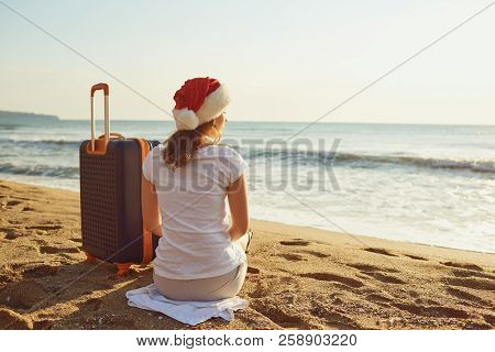 A Girl In A Santa Claus Hat With A Suitcase On The Beach On Chri