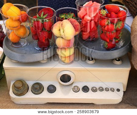 Vintage Scales With Filled Glasses Of Fresh Apricots Strawberries Peaches And Cucumber