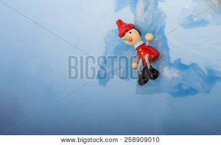 Hand Holding Wodden Puppet Pinocchio On In Blue Water