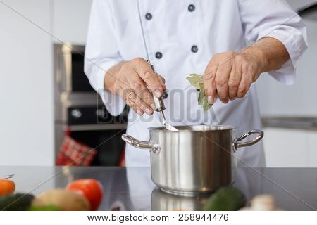 The Aged Chef Cooking A Soup In The Kitchen. The Concepy Of Cooking