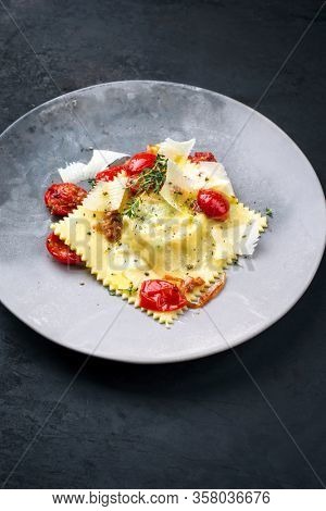 Traditional Italian ravioli pasta offered with parmesan cheese and fried tomatoes as closeup on a modern design plate 