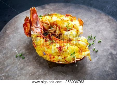 Traditional barbecue spiny lobster tail sliced and offered with saffron lemon sauce as closeup on a rustic modern design plate