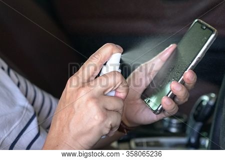 Man Spray Sanitizer Liquid Onto His Cellphone. Stay Healthy Or Kill Virus Or Bacteria Concept.
