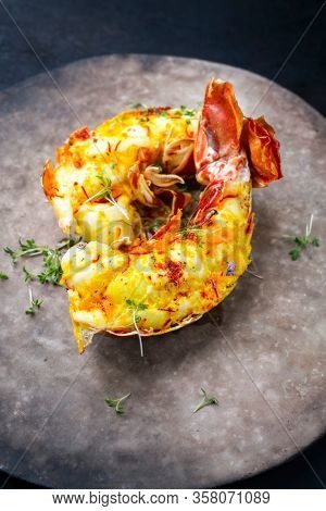Traditional barbecue spiny lobster tail sliced and offered with saffron lemon sauce as closeup on a rustic modern design plate 