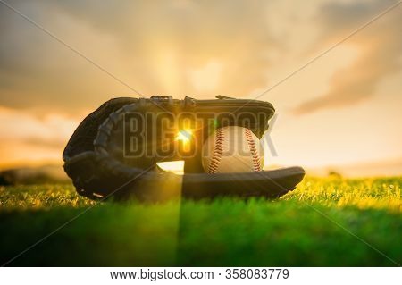 Baseball In Glove In The Lawn At Sunset In The Evening Day With Sun Ray And Lens Flare Light