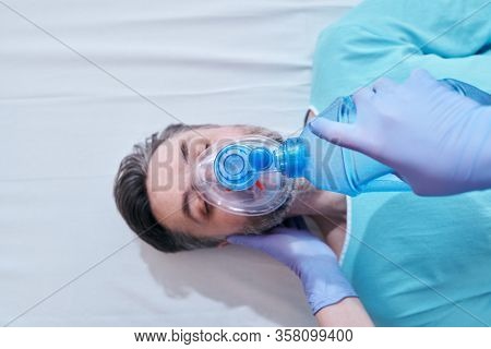 Above view of nurse in surgical gloves using Ambu bag for ventilation to ill mature patient
