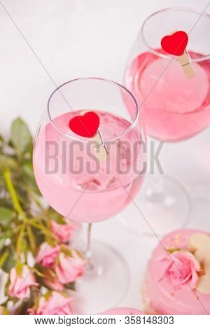 Two Glasses With Pink Grape Wine With Clothpin Heart Shaped And Roses On The Background. Romantic Di