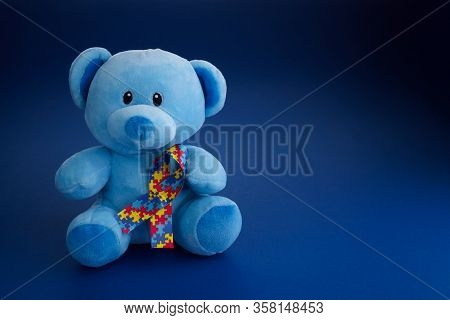 World Autism Awareness, Concept With Teddy Bear Holding Puzzle Or Jigsaw Pattern Ribbon On Blue Back