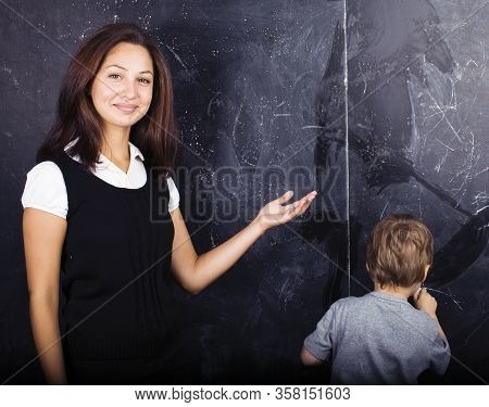 Little Cute Boy In Glasses With Young Real Teacher, Classroom Studying At Blackboard School Kido