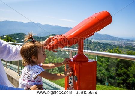 A Little Girl Looks Through Red Binoculars On A Viewing Platform With A Panorama Of The City. Large 