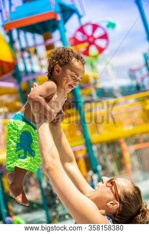 Little boy laughing with his mom at an outdoor water park during summer vacation. Smiling and having fun together. Cute, happy expression by a diverse bi-racial child in a vacation lifestyle photo.