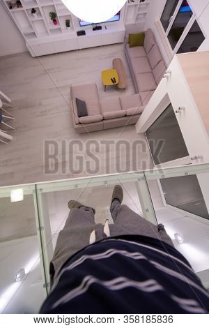 man standing upstairs on glass floor while looking at the inside of a stylish duplex apartment