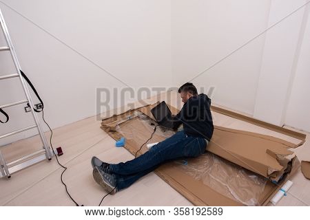 man checking business workflow using laptop computer while lying on floor with cardboard box placed below him during renovation of the apartment