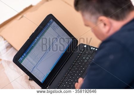 man checking business workflow using laptop computer while lying on floor with cardboard box placed below him during renovation of the apartment