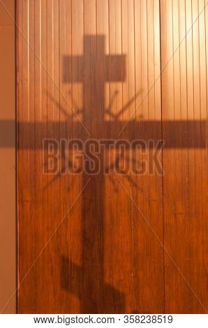 Shadow Of The Cross From The Setting Sun On Wall Of Wooden Panels.