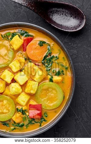 A Yellow Veg Thai Curry With Tofu And Vegetables In Black Bowl At Dark Slate Background. Vegetarian