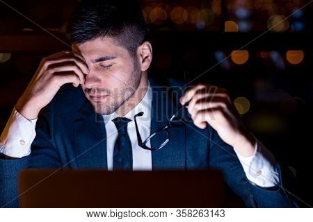 Headache And Stress. Businessman Massaging Nosebridge Holding Eyeglasses Sitting In Modern Office At