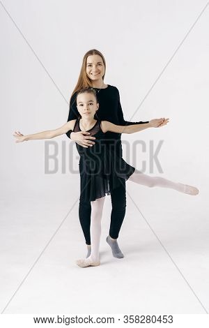 Mother Encourages Her Daughter Ballerina Sitting On The Floor On White Background.