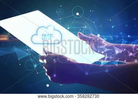 Hand holdig futuristic tablet with IMF inscription, modern technology concept