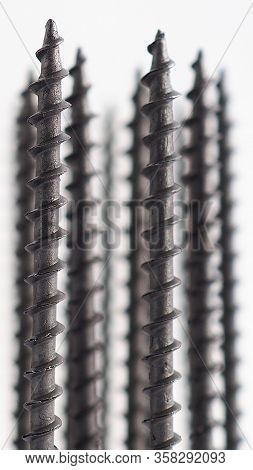 A Lot Of Black Long Screws Stand Upright On A White Background. Close-up. Hardware, Ironware, Ironmo