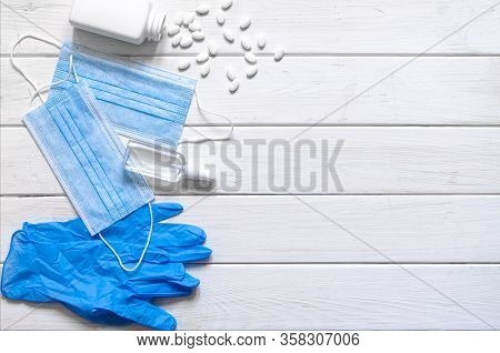 Medical Protective Mask, Rubber Gloves, Antiseptic And White Anti-irus Tablets Lie On A White Wooden