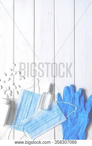 Medical Protective Mask, Rubber Gloves, Antiseptic And White Anti-irus Tablets Lie On A White Wooden
