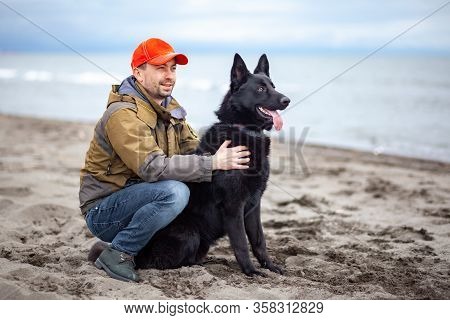 German Black Shepherd With Its Owner On The Sandy Beatch Of Black Sea