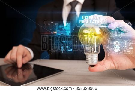Businessman holding lightbulb with INTERNET REGULATION inscription, online security idea concept