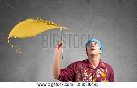 Young Artist Painting Yellow Brush Stroke. Male Painter In Dirty Shirt And Bandana With Paintbrush O