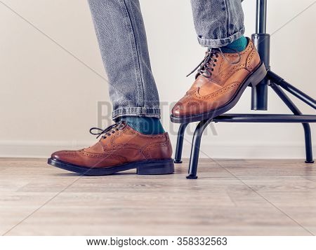 A Man In Brown Brogs And Blue Socks Sits On A Chair