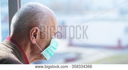 Elderly Man In Protective Face Mask Against Virus Looks Out Window Stay At Home