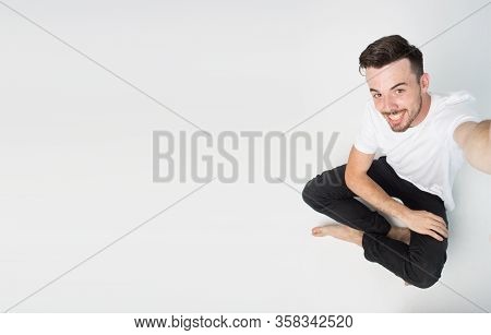 Young Man Isolated Over Background. Guy Sit On Floow And Take Selfie Alone. Side View Of Emotional G