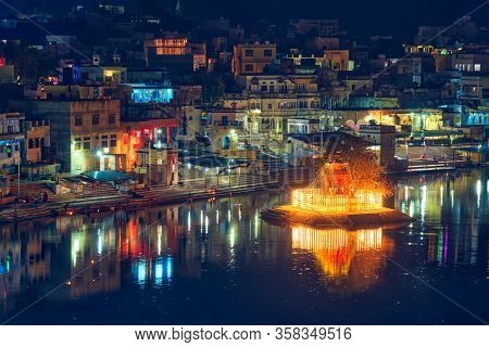 View of famous indian hinduism pilgrimage town sacred holy hindu religious city Pushkar with Brahma temple, aarti ceremony, lake and ghats illuminated at sunset. Rajasthan, India. Horizontal pan