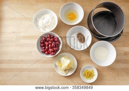 Ingredients In White Bowls To Bake A Cherry Cake In A Springform Pan On A Wooden Kitchen Countertop,