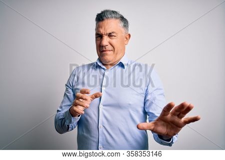 Middle age handsome grey-haired business man wearing elegant shirt over white background disgusted expression, displeased and fearful doing disgust face because aversion reaction. With hands raised