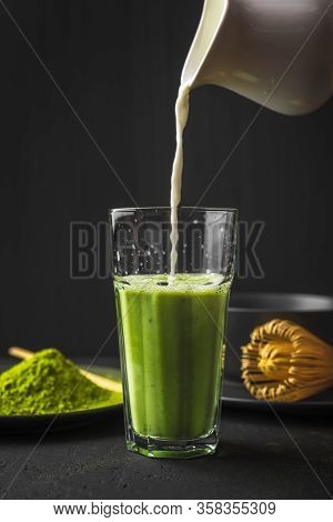 Matcha Green Tea Powder Latte With Milk In Two High Glass On Stone Table, Process Of Pouring Milk In