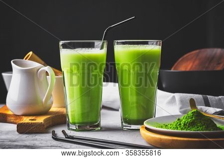 Matcha Green Tea Powder Latte With Milk In Two High Glass On Stone Table, Black Straw, Wooden Plate 