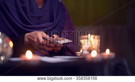 Close-up of soothsayer woman guessing on cards sitting at table with burning candles, magic ball