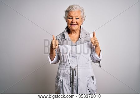 Senior beautiful grey-haired woman wearing casual jacket standing over white background success sign doing positive gesture with hand, thumbs up smiling and happy. Cheerful expression and winner 