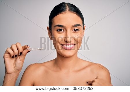 Young beautiful brunette woman holding dental aligner orthodontic to teeth corretion with surprise face pointing finger to himself