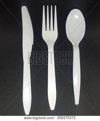 White Plastic Cutlery On A Black Background, Knife, Fork And Spoon