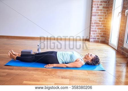 Middle age beautiful sportwoman lying down on mat practicing yoga doing corpose pose at gym
