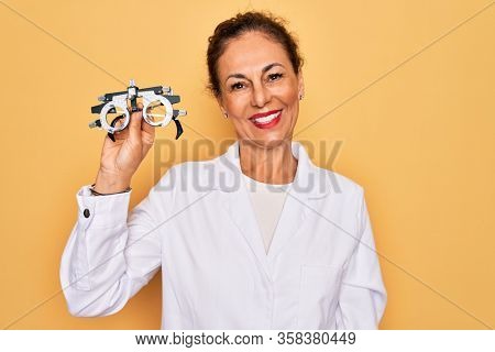 Middle age senior oculist woman holding optometrical glasses for vision correction with a happy face standing and smiling with a confident smile showing teeth