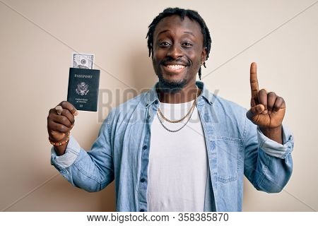 Young african american tourist man holding passport with dollars banknotes as money travel surprised with an idea or question pointing finger with happy face, number one