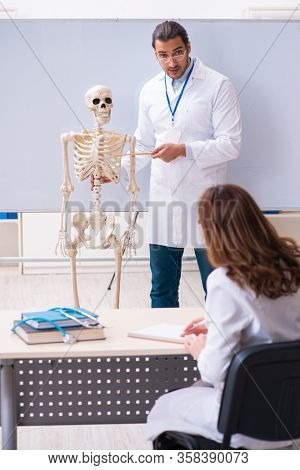 Young male teacher doctor, skeleton and female student in the cl